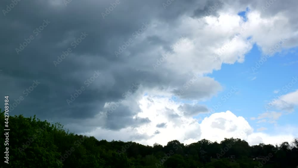 Massive dark rain clouds move into the shot from the left above the hill
