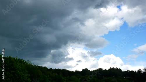 Massive dark rain clouds move into the shot from the left above the hill
