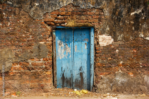 A rustic blue wooden door in an old, ruined laterite brick wall in the heritage town of Fort Kochi.