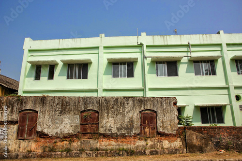Vintage windows on rusty decaying brick wall with a modern concrete building behind in the heritage town of Mattancherry.