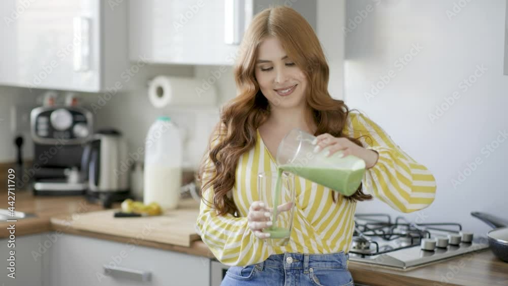 Young woman in kitchen pouring green smoothie in glass Young woman in kitchen pouring green smoothie in glass