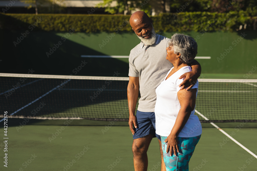 Portrait of smiling senior african american couple embracing on tennis court