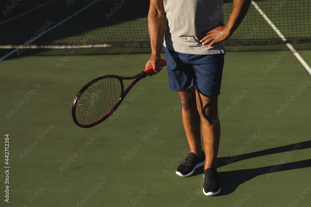 Midsection of senior african american man holding tennis racket on tennis court