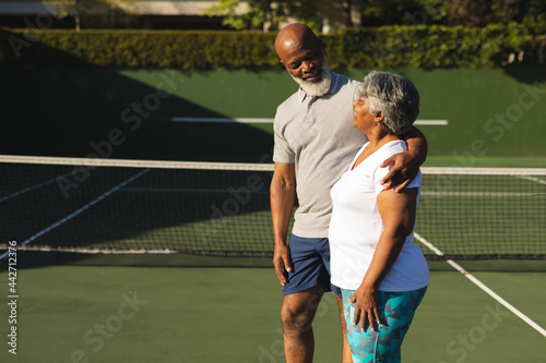 Portrait of smiling senior african american couple embracing on tennis court