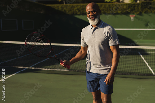 Smiling senior african american man playing tennis on tennis court