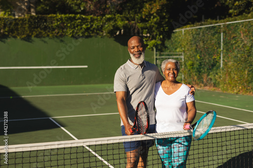 Portrait of smiling senior african american couple with tennis rackets on tennis court