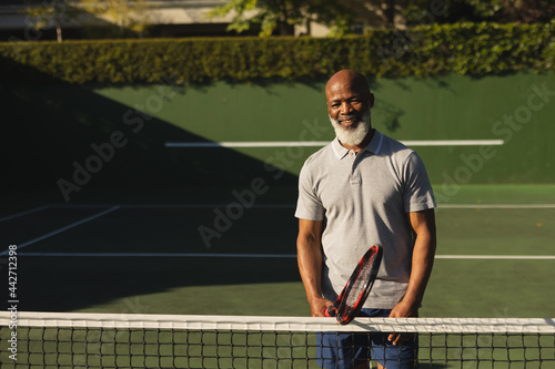Portrait of smiling senior african american man holding tennis racket on tennis court