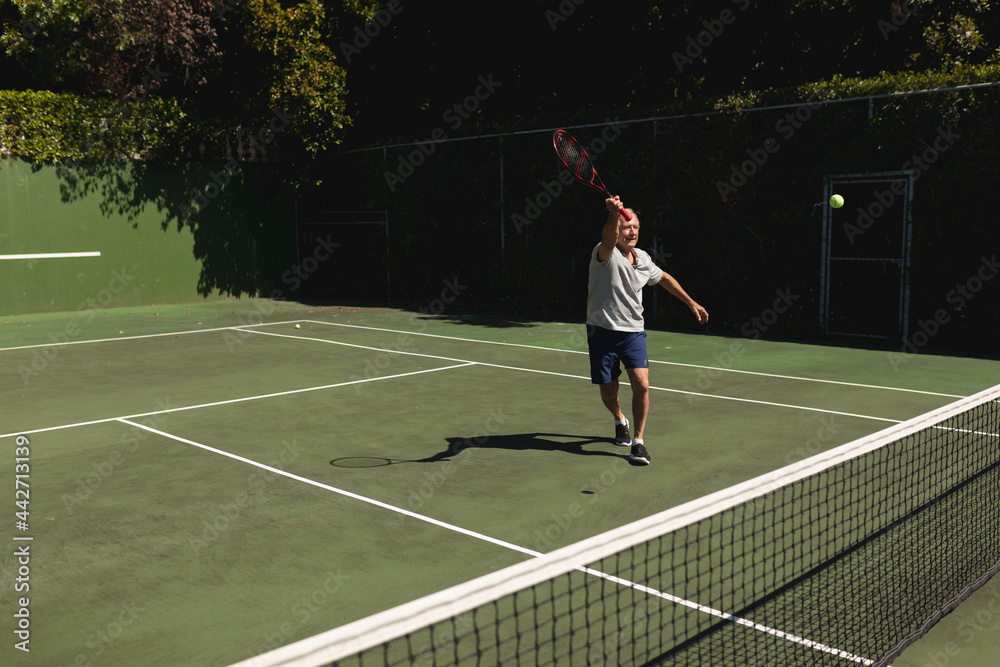 Senior caucasian man playing tennis on court holding tennis racket