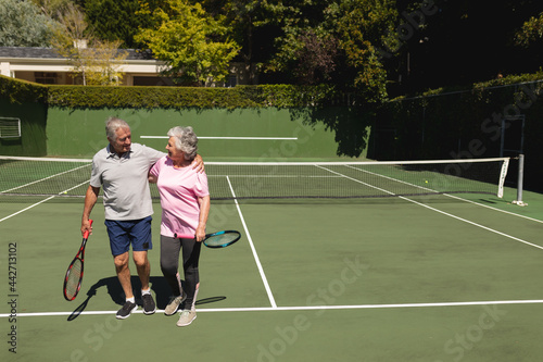 Senior caucasian couple embracing and smiling on tennis court