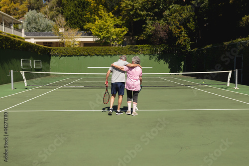 Senior caucasian couple embracing and walking on tennis court