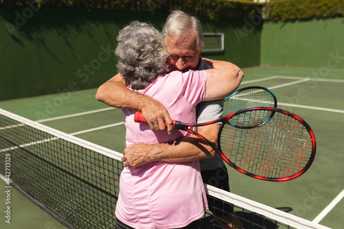 Senior caucasian couple playing tennis together on court embracing