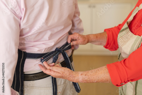 Mid section of senior caucasian couple tying apron in kitchen