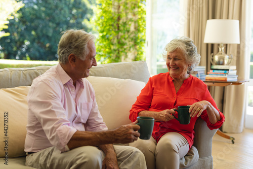 Senior caucasian couple sitting on sofa together drinking coffee in living room