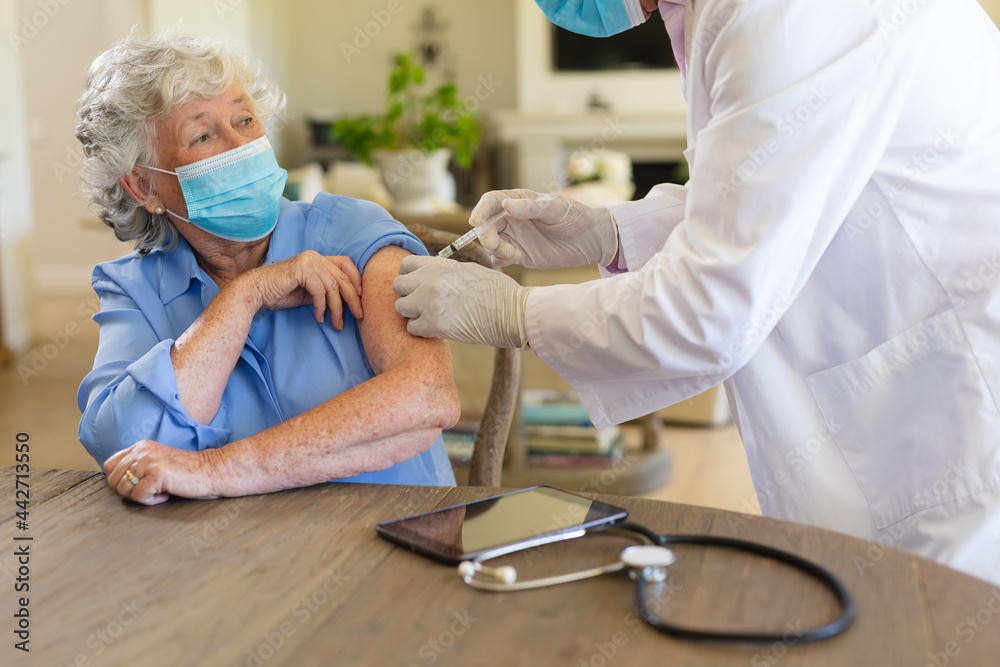 Obraz premium Senior caucasian male doctor vaccinating female patient wearing face masks