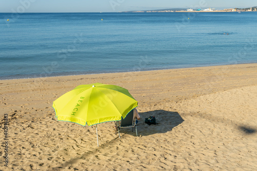 Unrecognizable person under a yellow umbrella on a beach on the island of Mallorca at sunrise