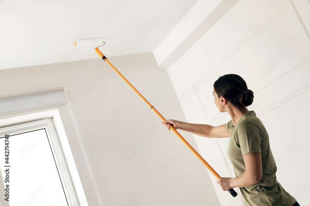 Young woman painting ceiling with white dye indoors, space for text Young woman painting ceiling with white dye indoors, space for text