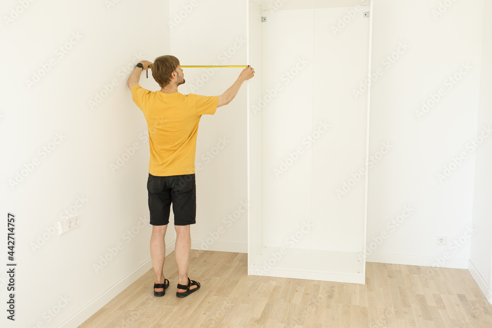Hands holding a tape measure Man measuring white wall in new apartment. Wardrobe system design in a flat. Storage in room. Male with ruler. Furniture assembling and installation at living room cabinet