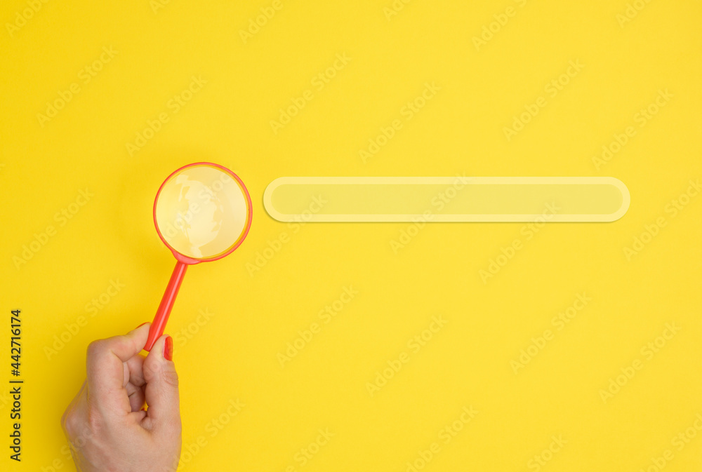 a female hand holds a red plastic magnifying glass on a yellow background a female hand holds a red plastic magnifying glass on a yellow background