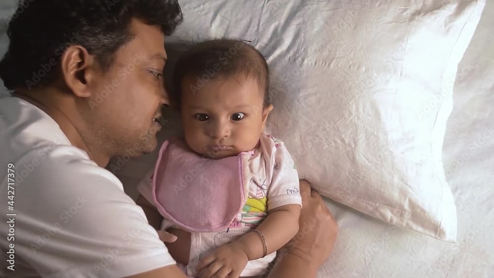 Happy Baby Loves Daddy Kisses. Loving Father kissing cute little adorable kid on bed. Close-up portrait. Indian ethnicity. Side view. Happy parents day Fatherhood parenthood togetherness background.