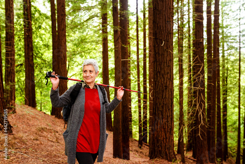 senior woman in a redwood forest with a trekking pole across her shoulders. Mature person hiking.