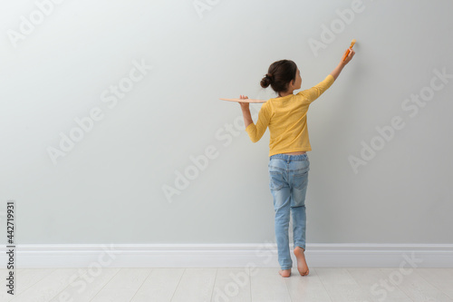 Little girl painting on light grey wall indoors, back view. Space for text