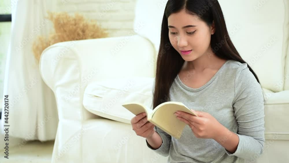 Young asian woman reading book on cozy couch sofa at warm hom. Relax woman holding book read on sofa near window happiness.woman reading open book leisure mind. Happiness woman lifestyle at home