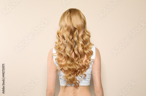 Young woman with long curly hair on beige background, back view