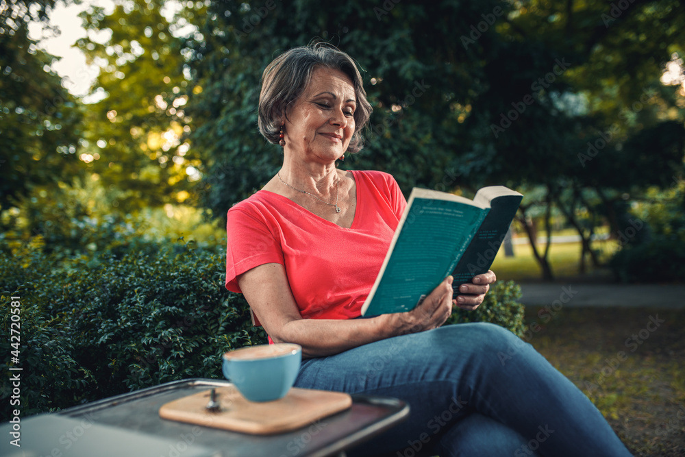 Fototapeta premium Senior woman reading book in outdoor coffee shop.