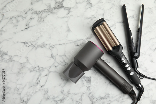 Fotografie Hair dryer, straightener and triple curling iron on white marble background, flat lay