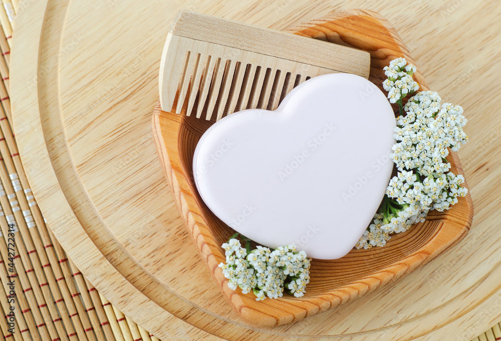 Small wooden plate with heart shaped pink bar of soap (solid shampoo),  yarrow flowers and wooden hair brush. Natural beauty treatment, hair care  or zero waste concept. Top view, copy space. Stock