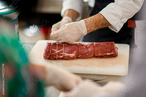 Tablou pe pânză Close-up view of meat and chef's hands which tie it with butcher's twine
