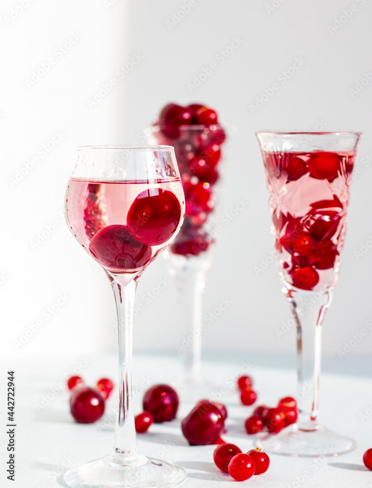set of glasses of pink gin or vodka infused with cranberry among frozen berries, a long-stemmed crystal glasses with cherry liqueur or any red alcoholic cocktail on light blue background, minimalism set of glasses of pink gin or vodka infused with cranberry among frozen berries, a long-stemmed crystal glasses with cherry liqueur or any red alcoholic cocktail on light blue background, minimalism