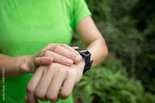 Asian woman ultramarathon runner set the smartwatch before running at tropical rainforest trail