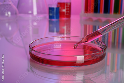Dripping red reagent into Petri dish with sample on table, closeup