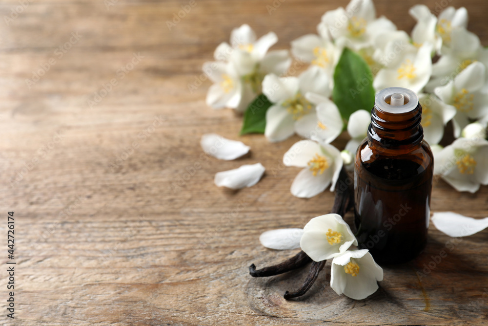 Jasmine essential oil and fresh flowers on wooden table, space for text