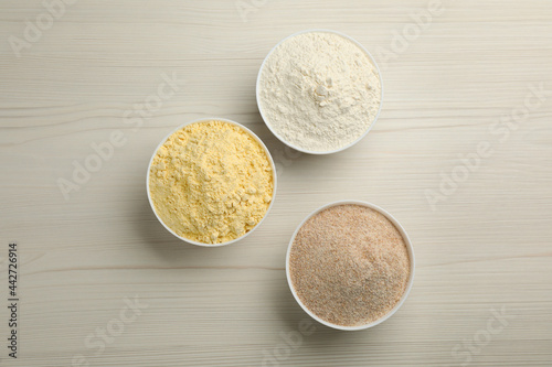 Different types of flours in bowls on white wooden table, flat lay