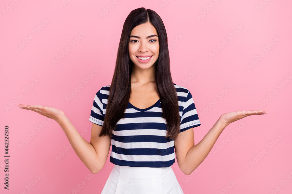 Photo portrait of girl in striped t-shirt smiling comparing copyspaces holding on hands isolated on pastel pink color background Photo portrait of girl in striped t-shirt smiling comparing copyspaces holding on hands isolated on pastel pink color background