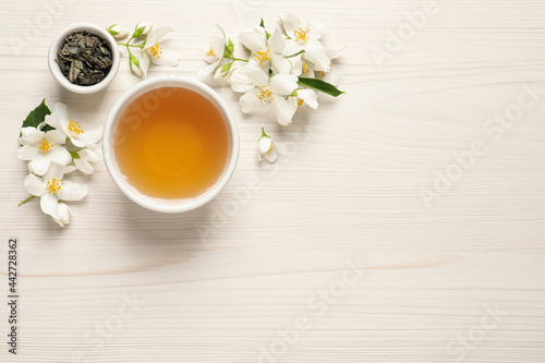 Aromatic jasmine tea, dry leaves and fresh flowers on white wooden table, flat lay. Space for text