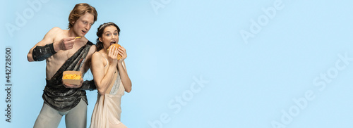 Burger and fast food. Young couple of ballet dancers in ancient Rome costums at blue studio.