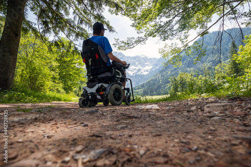 Man on a wheelchair relaxing in nature and looking at mountains on a sunny summer day.