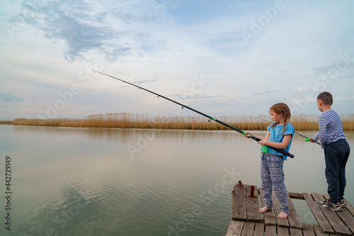 little girl and boy fish on a fishing rod standing on a wooden bridge. fishermen