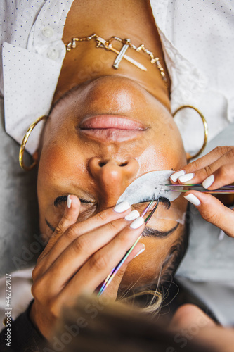 Crop beautician applying eyelashes on face of black woman