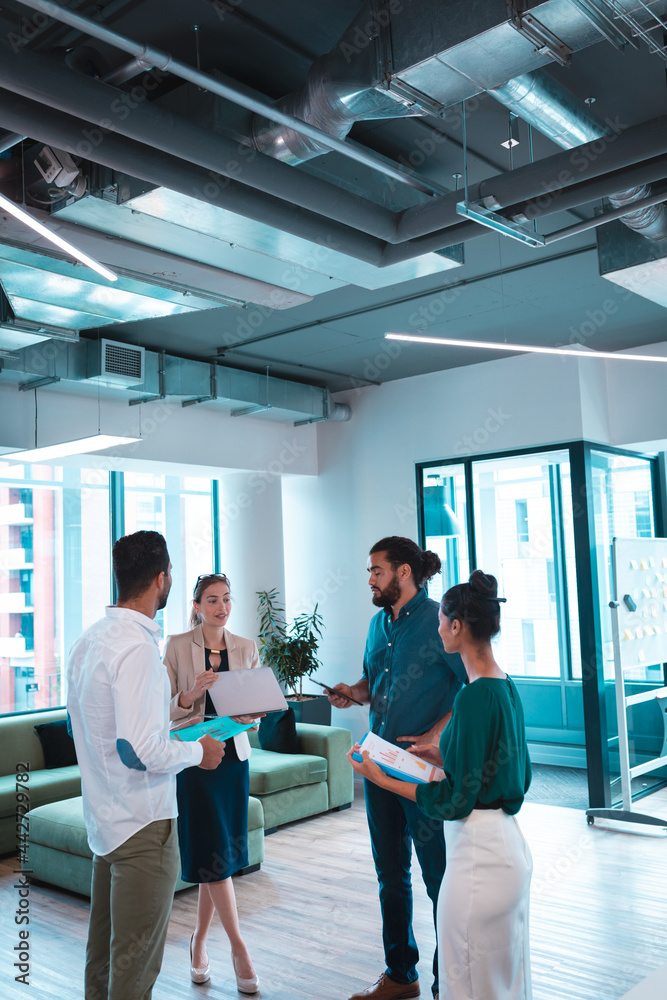 Group of diverse businesspeople discussing together and holding documents and laptop Group of diverse businesspeople discussing together and holding documents and laptop