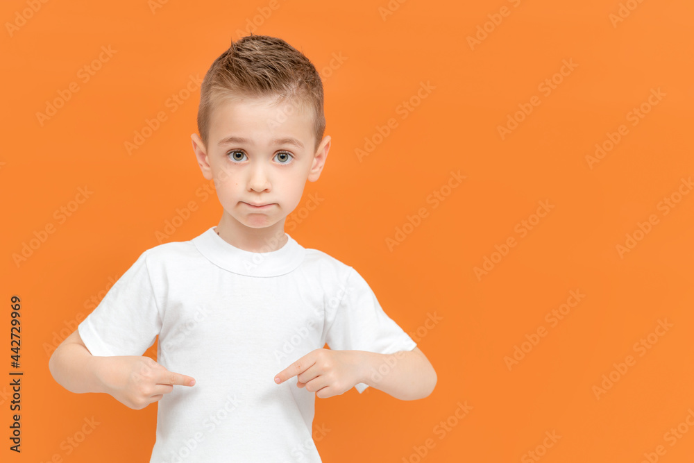 Funny little boy isolated on orange background pointing by hand to a white t-shirt copy space. Mockup for design Funny little boy isolated on orange background pointing by hand to a white t-shirt copy space. Mockup for design