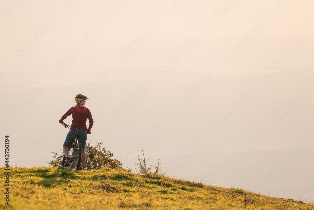 Wide shot, back view of silhouette sitting on a mountain bike, enjoying an amazing view