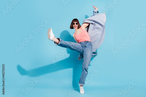 Photo of adorable cool young lady dressed jeans shirt dark glasses smiling dancing walking isolated blue color background