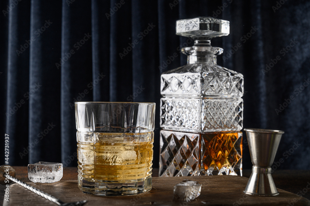 Whiskey in rocks and bottle on dark blue curtain background. Holiday party. Close up.