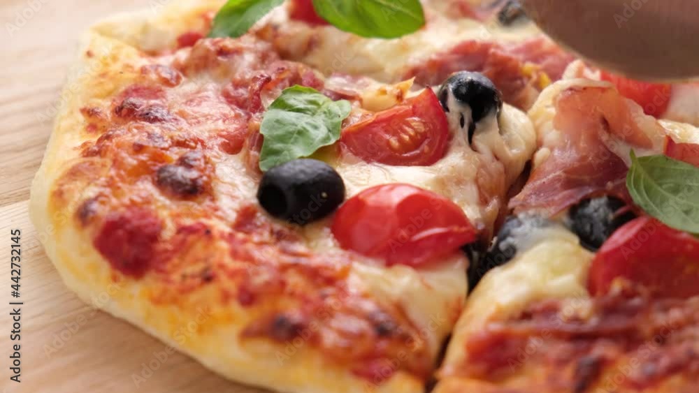 Closeup view slicing pizza with pizza cutter knife. Delicious hot pizza with tomato, olives, cheese and ham Closeup view slicing pizza with pizza cutter knife. Delicious hot pizza with tomato, olives, cheese and ham
