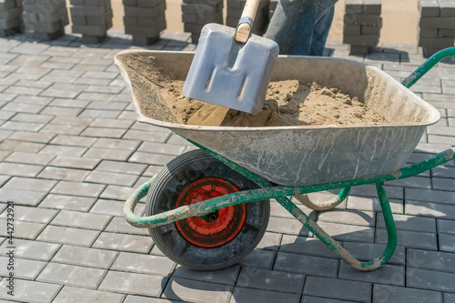 Fotografie, Obraz Close-up of a worker using a shovel and filling a wheelbarrow with sand to build a sidewalk road