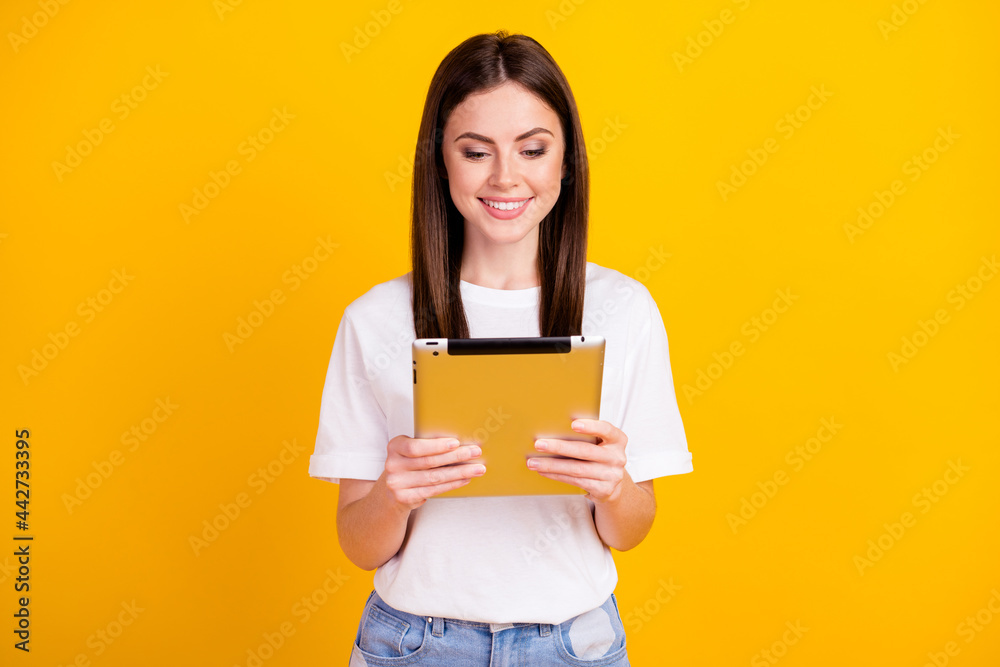 Photo of young girl happy positive smile look read browse tablet isolated over yellow color background Photo of young girl happy positive smile look read browse tablet isolated over yellow color background
